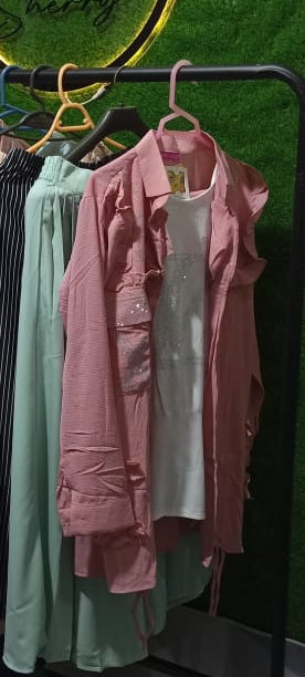 Clothing rack with various shirts against a green wall with 'Goon' sign.
